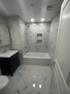 Small white bathroom with tub-shower, sink vanity, toilet, and marble-pattern tile floor and walls