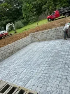 Concrete foundation area with block retaining wall and two red trucks on a grassy slope above
