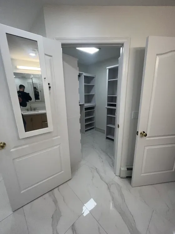 Open closet with white shelves and mirrored doors in a bright tiled room