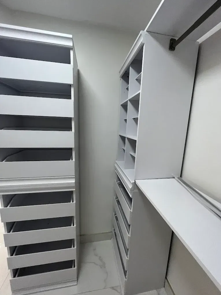White walk-in closet with shelving, drawers, and hanging rods in a narrow hallway