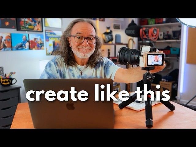 A man is holding a camera in front of a laptop that says create like this