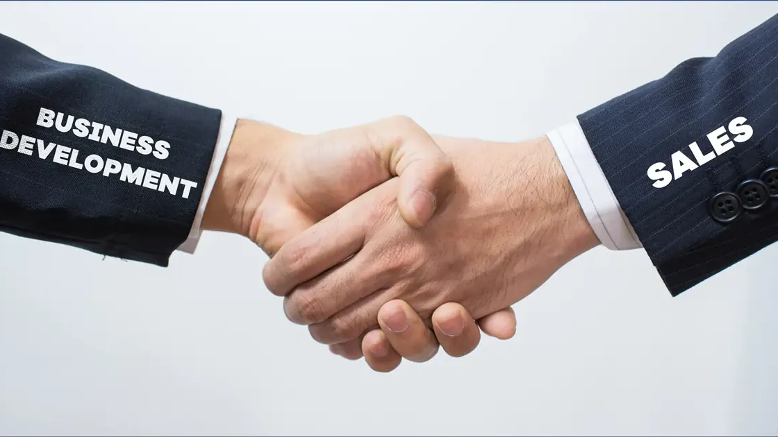 Two men are shaking hands with business development and sales written on their sleeves.