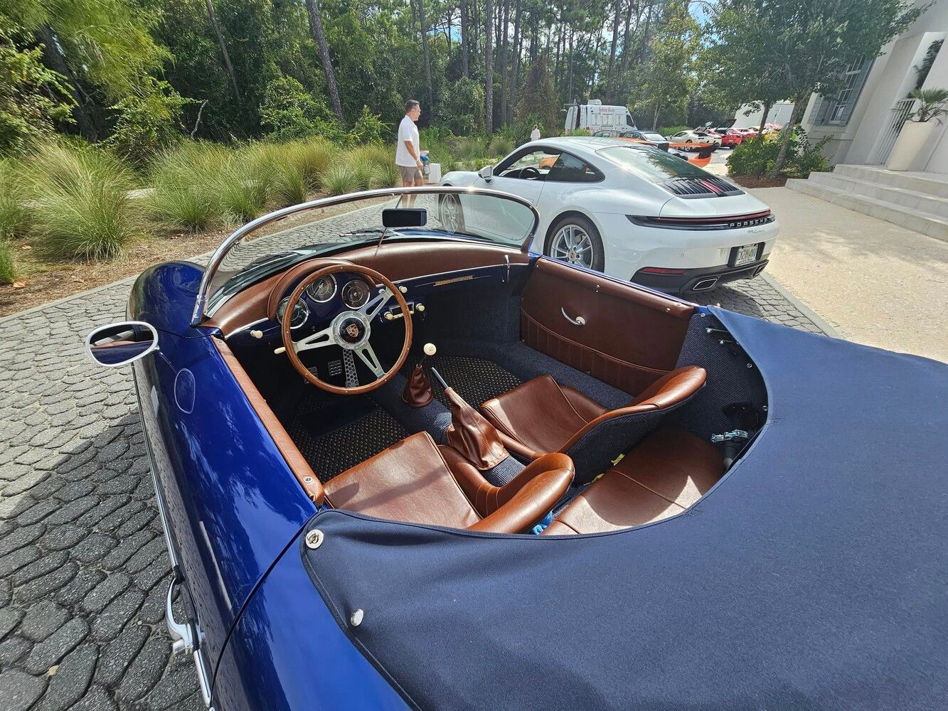 Blue convertible Porsche, tan interior, parked with a white Porsche coupe on a sunny day.
