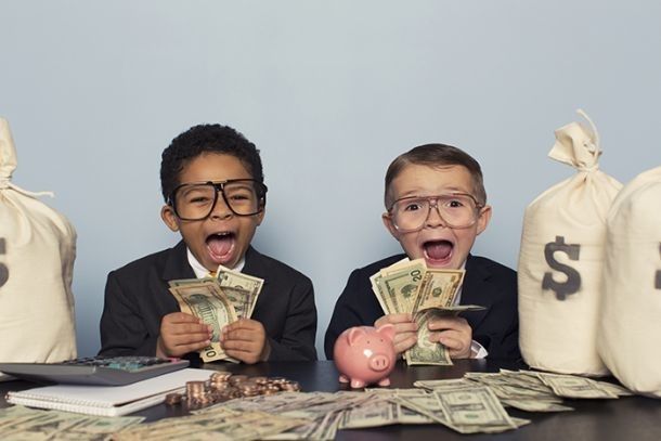 Two children in suits with glasses holding money, excitedly surrounded by cash and money bags.