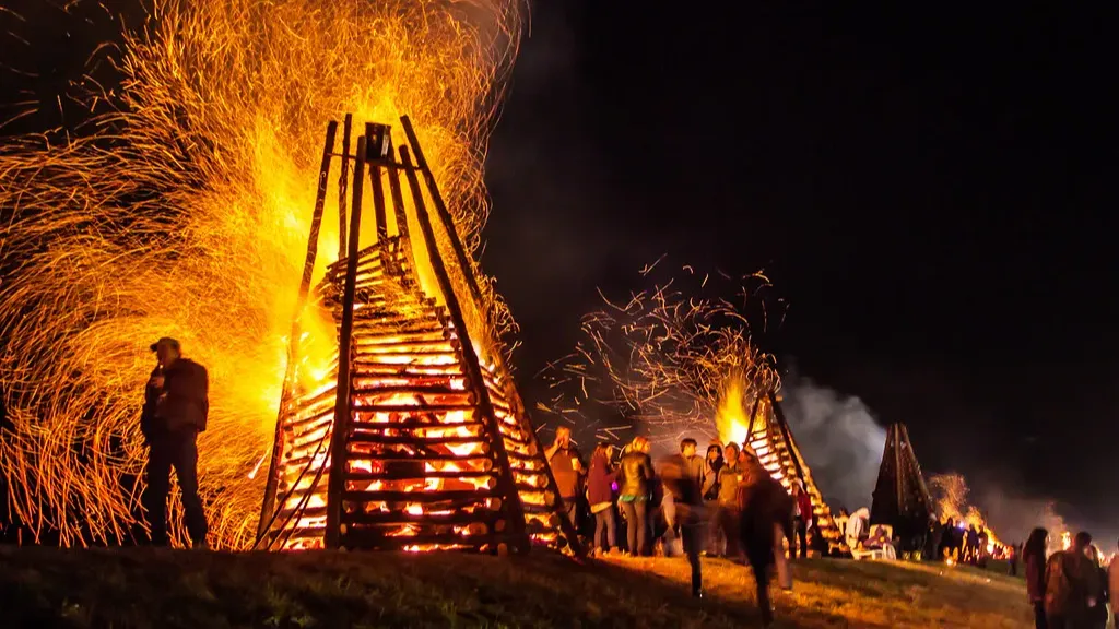 Large bonfires ablaze at night with people watching. Sparks fly into the dark sky.