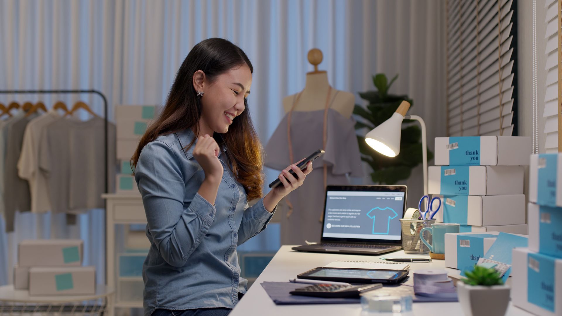 A woman is sitting at a desk using a cell phone.