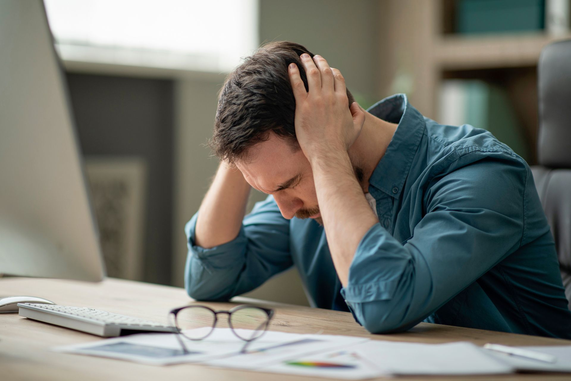 A man is sitting at a desk with his head in his hands.