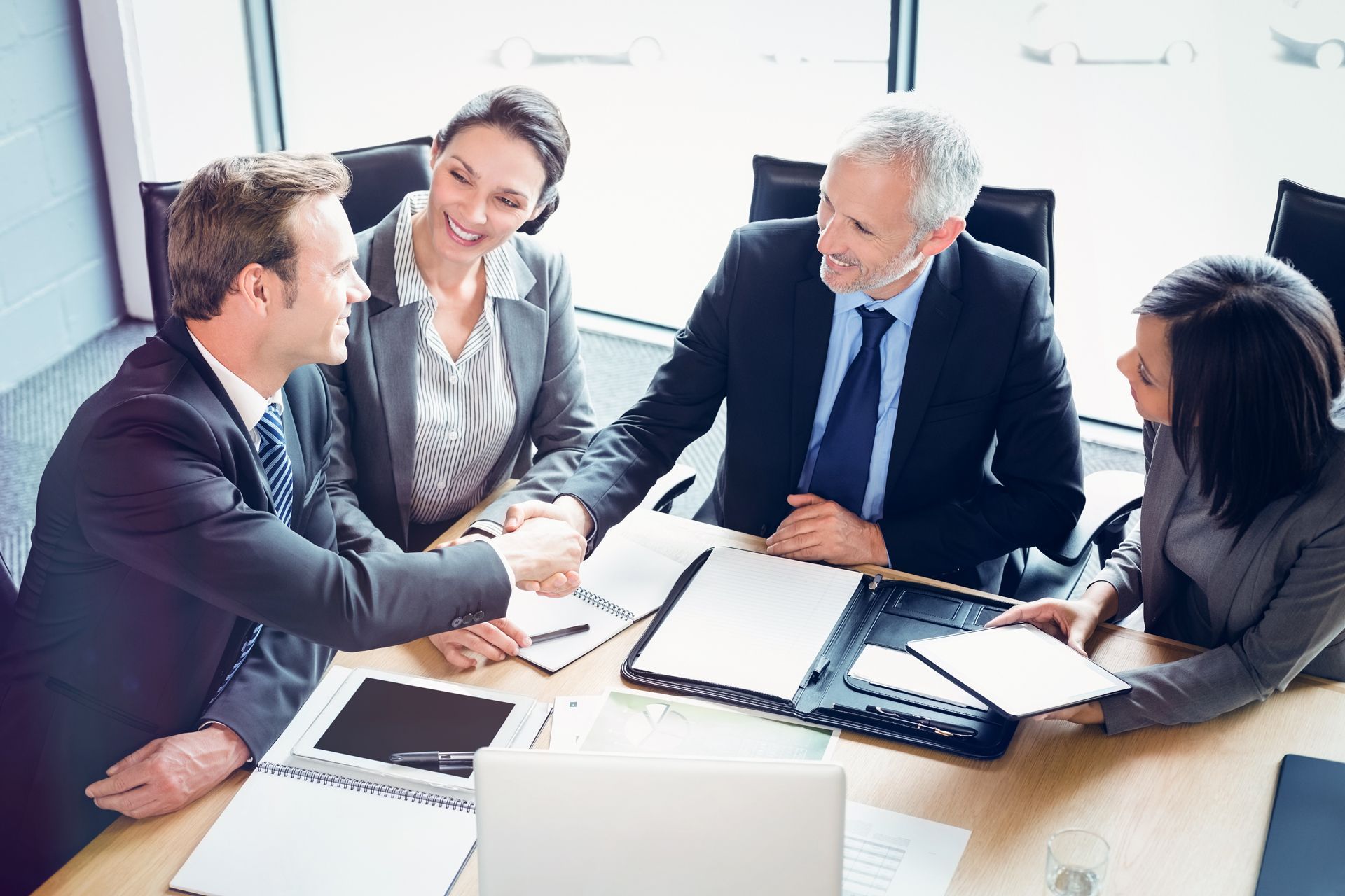 a group of business people are sitting around a table shaking hands