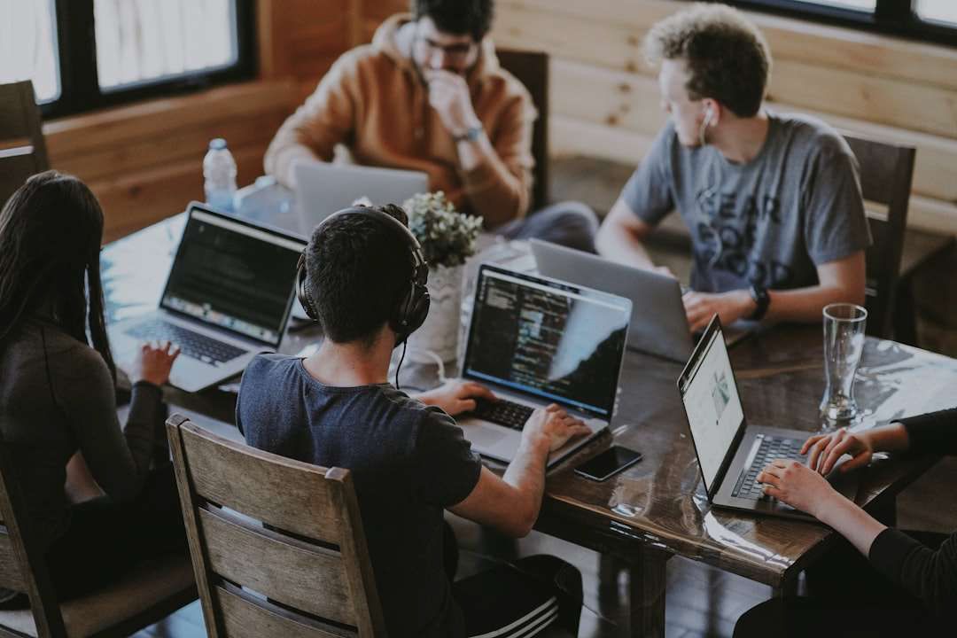 A group of people are sitting around a table with laptops.