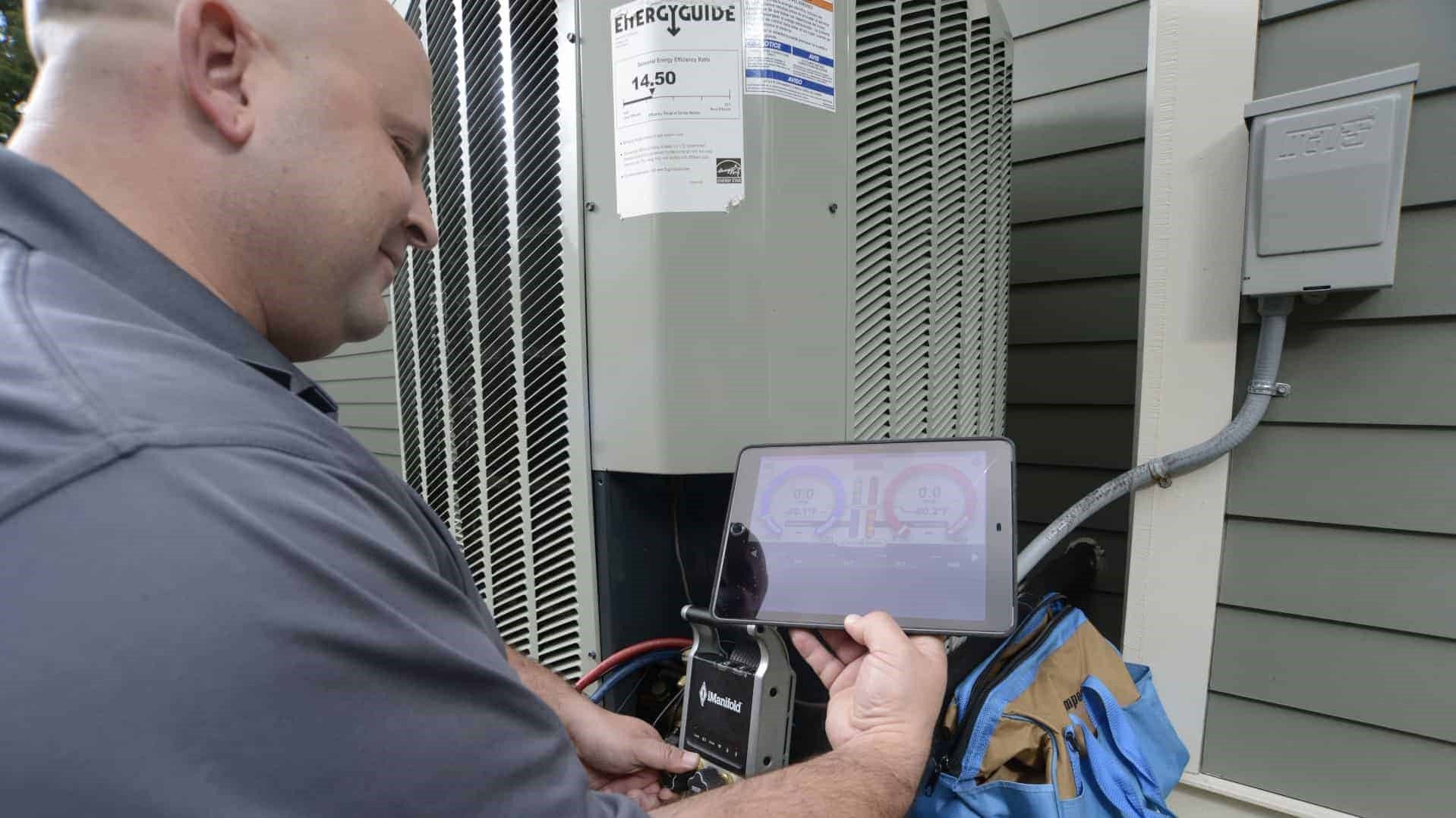 A man is working on an air conditioner with a tablet.