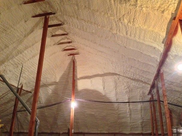 A man is kneeling down in an attic holding a tablet.