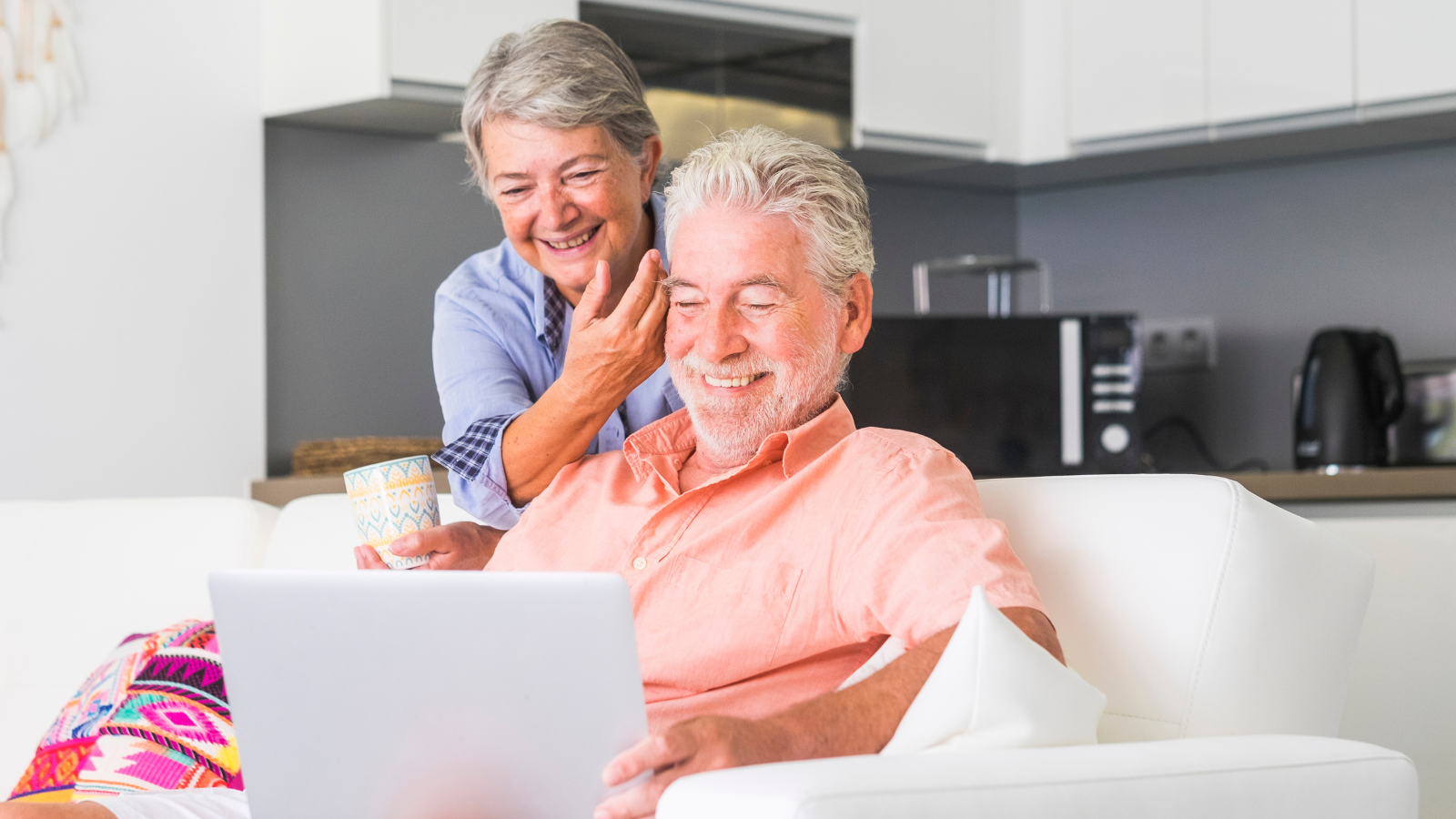 An elderly couple is sitting on a couch using a laptop computer.