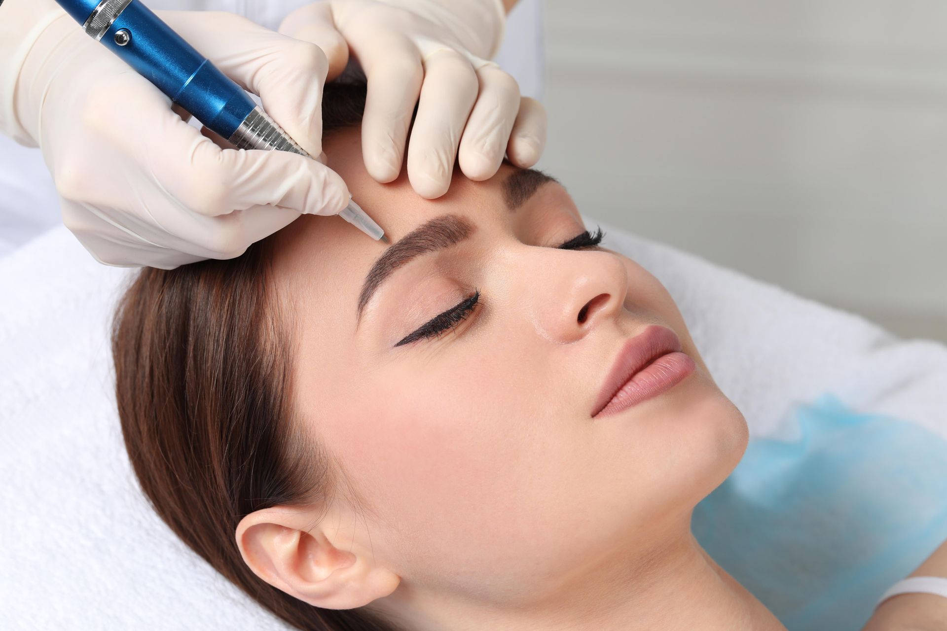 A woman is getting a permanent eyebrow tattoo on her forehead.