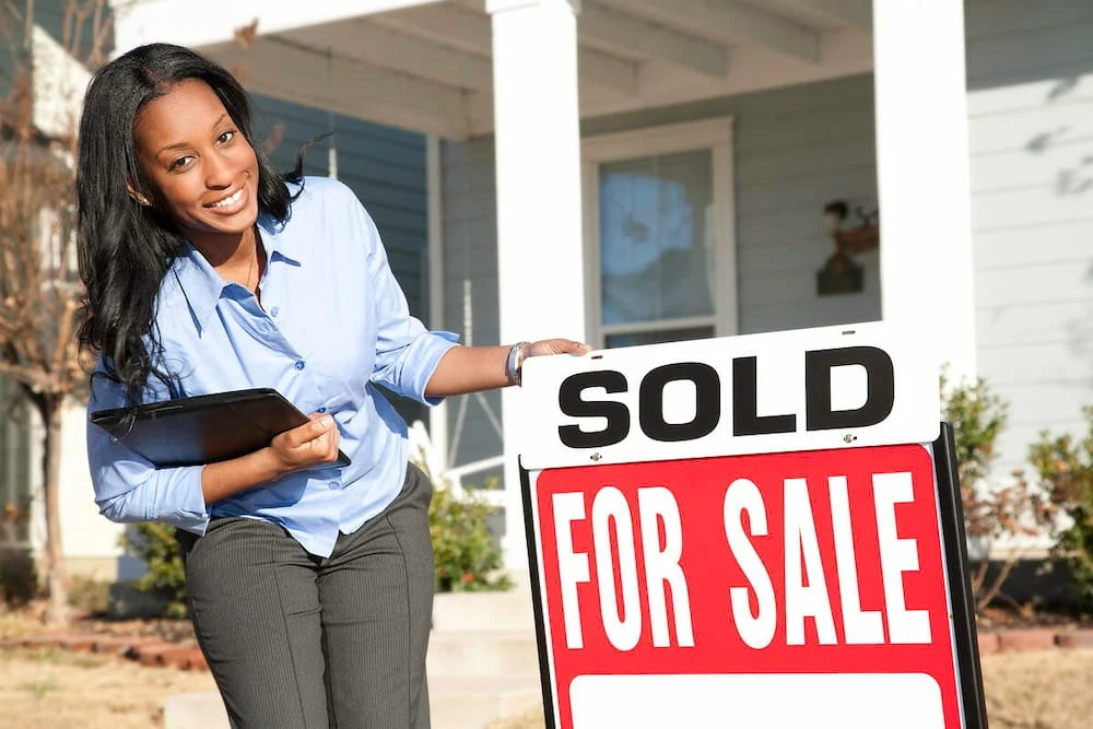 A woman is standing next to a sold for sale sign