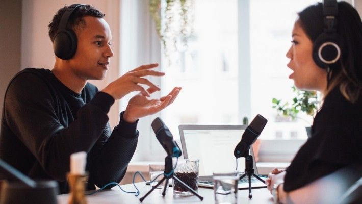 A man and a woman are sitting at a table talking into microphones.