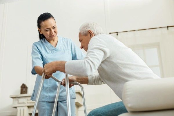 A nurse is helping an elderly man use a walker.