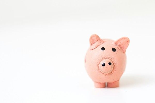 A pink piggy bank with black eyes is sitting on a white surface.