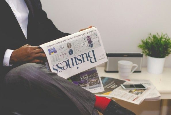 A man is sitting at a table reading a business newspaper.