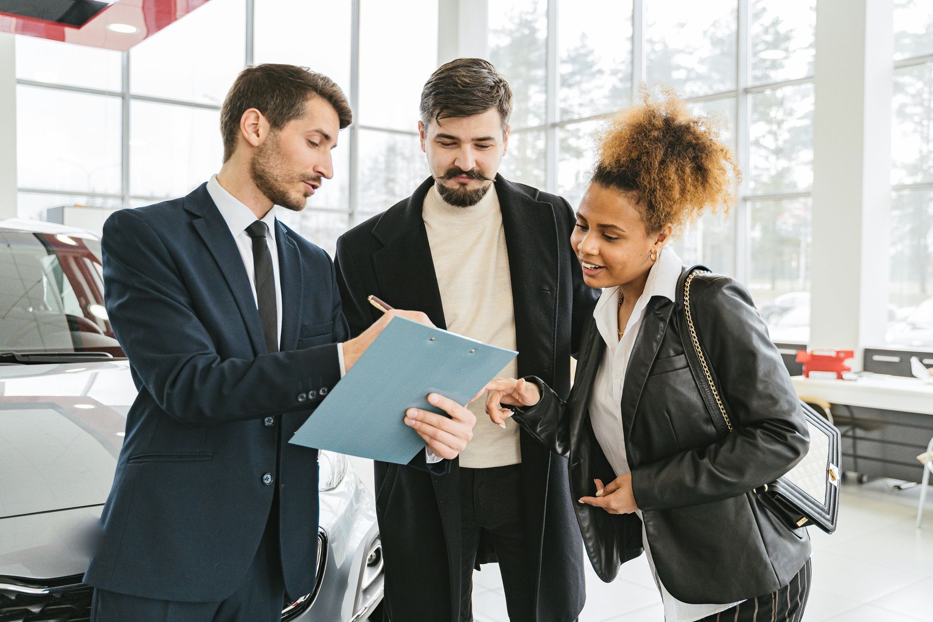 Car salesman showing paperwork to a couple inside a dealership, near a car.