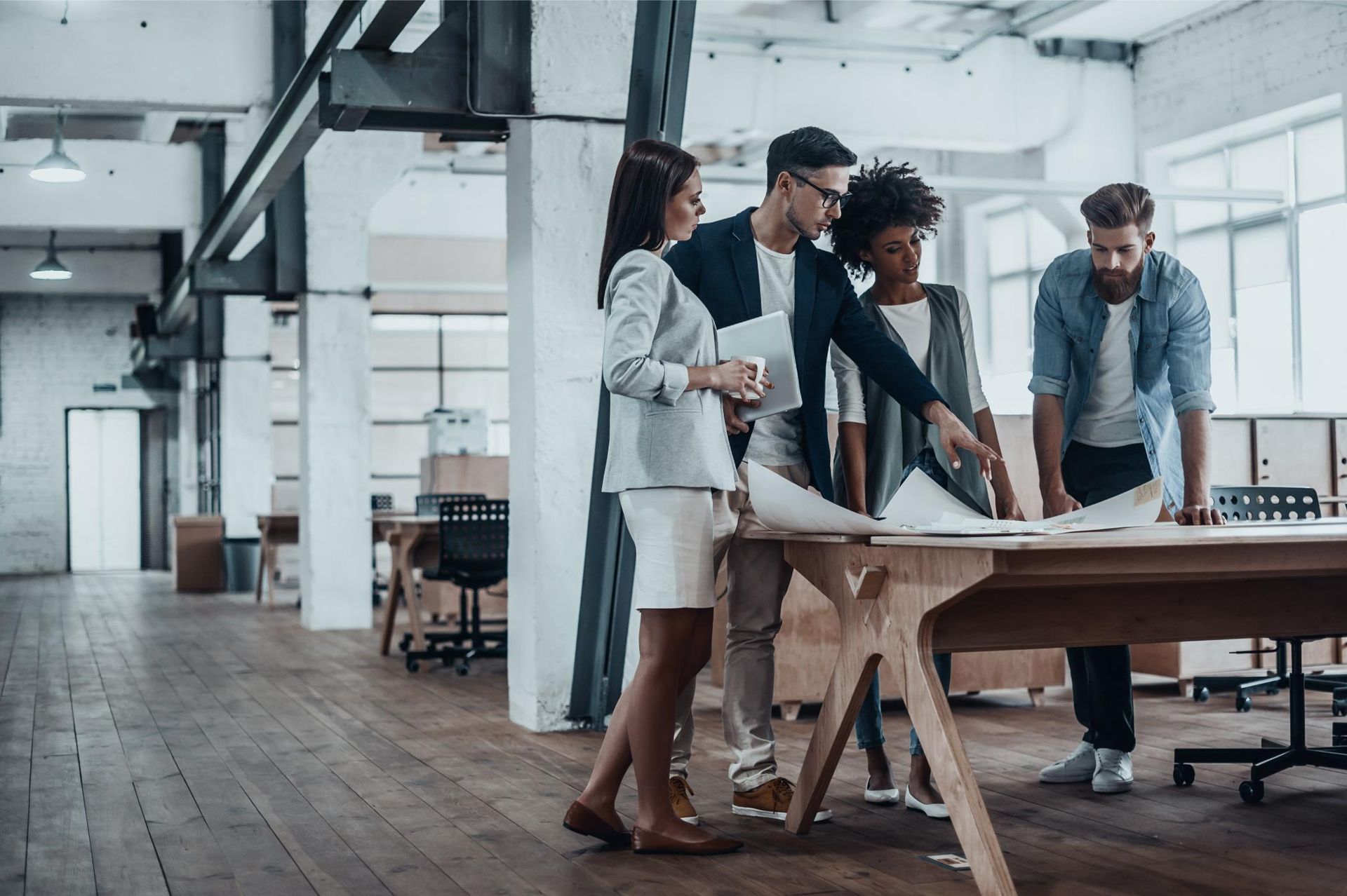 A group of people are standing around a table in an office looking at papers.