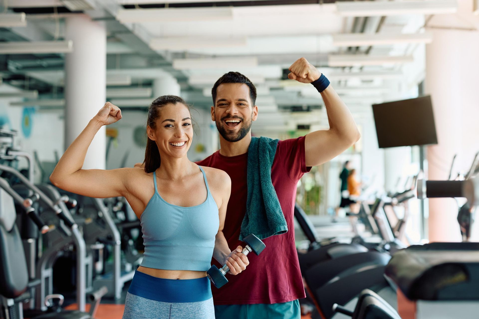 A man and a woman are flexing their muscles in a gym.