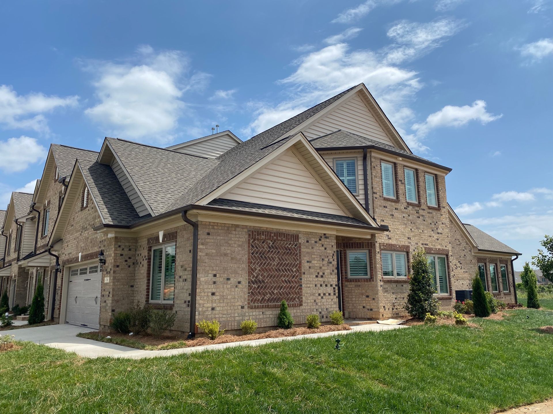 Multi-story brick townhouses with tan accents under a blue sky with some clouds.