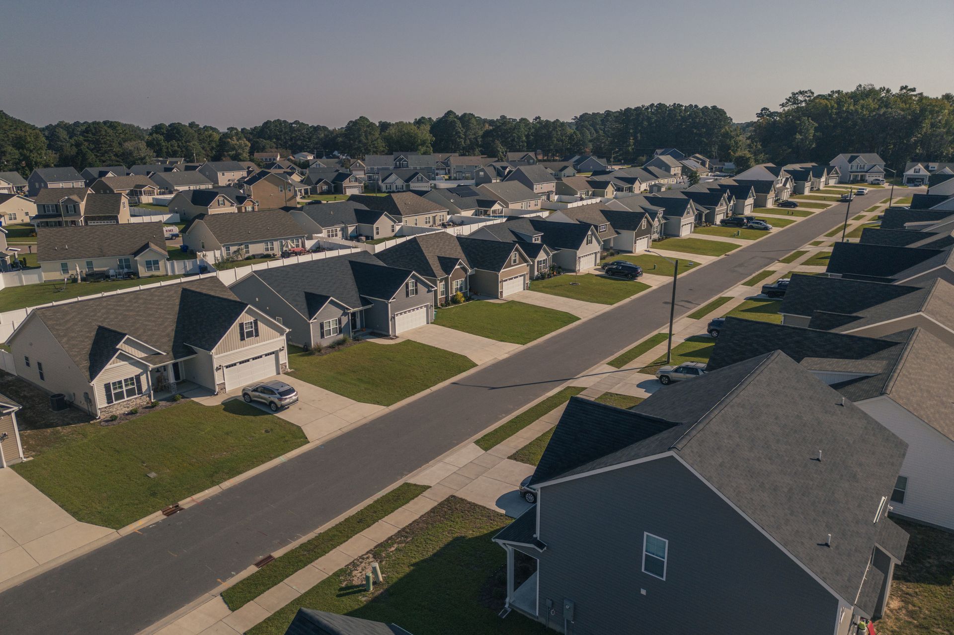 Aerial view of a suburban neighborhood with rows of houses, a street, and green lawns on a sunny day.