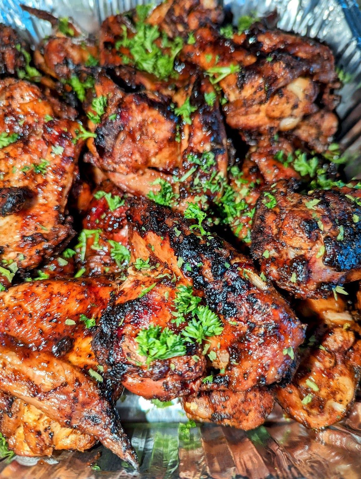 A close up of a tray of grilled chicken with parsley on top.