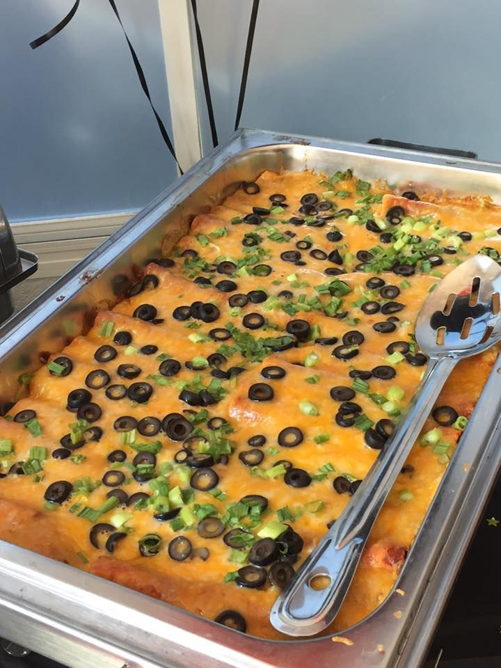 A casserole dish filled with enchiladas and olives with a spoon in it.