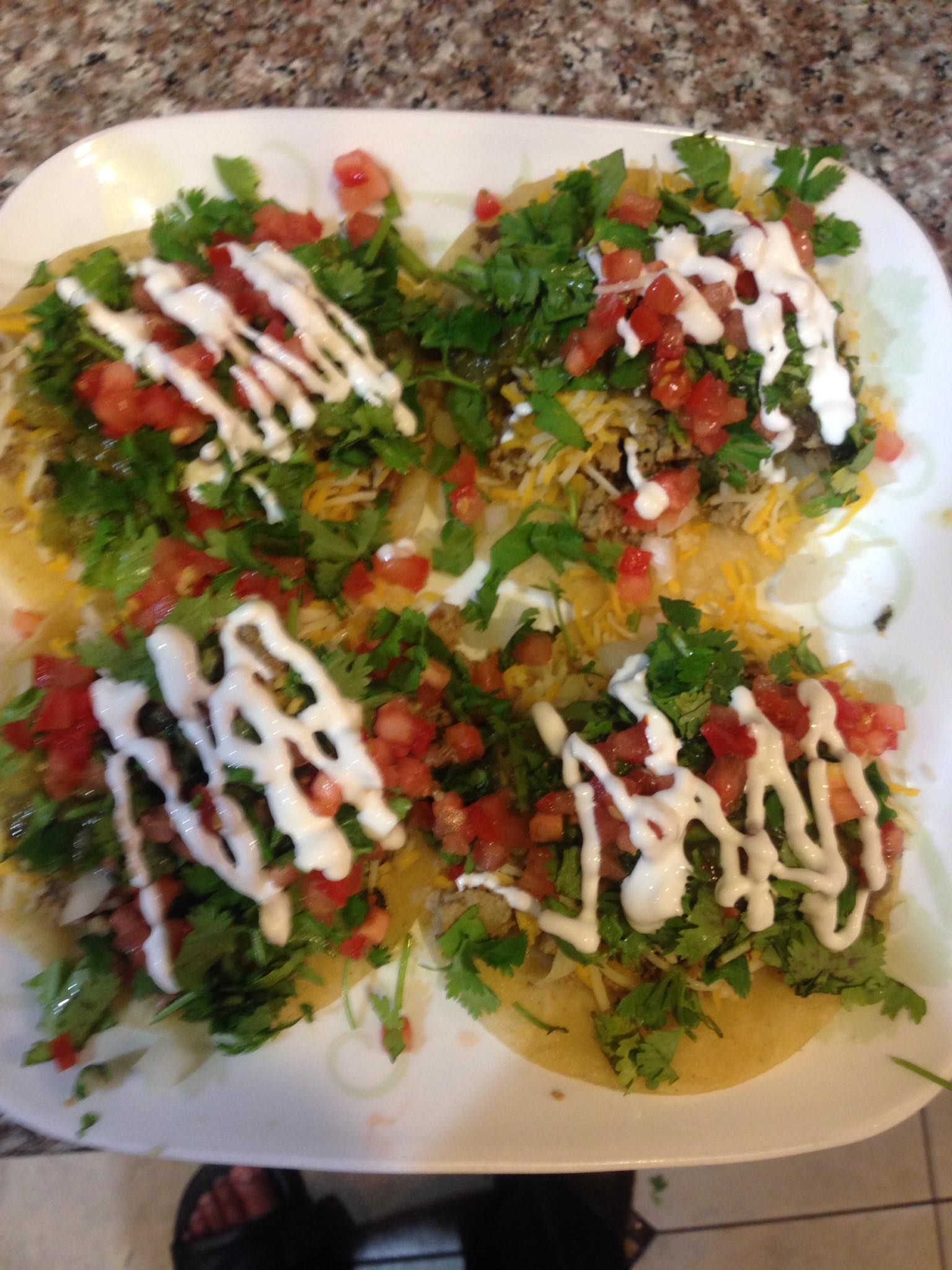 A white plate topped with four tacos with tomatoes , cilantro and sour cream.