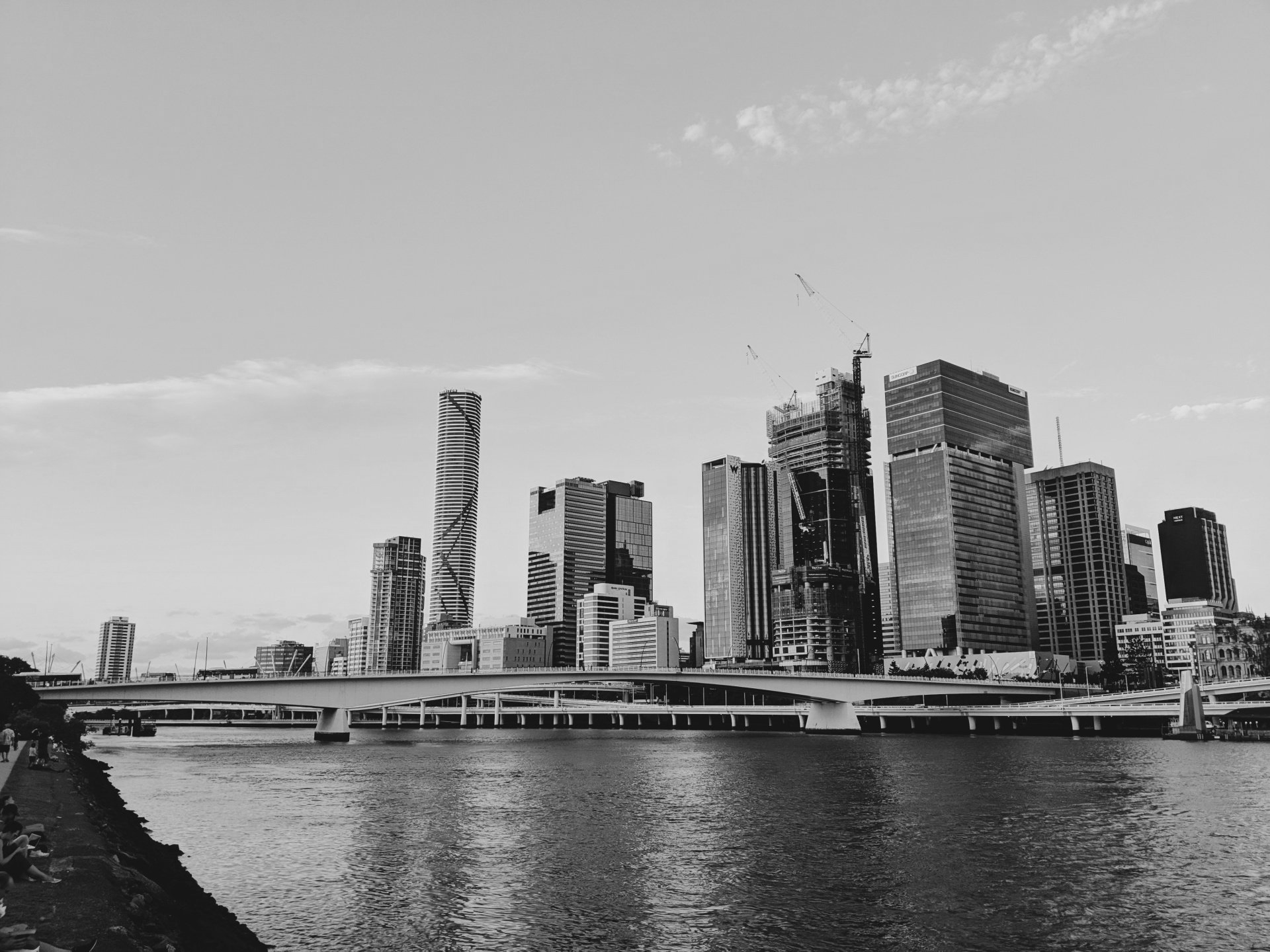 Paisagem urbana em preto e branco de Brisbane, Austrália, com edifícios, ponte e rio em primeiro plano.