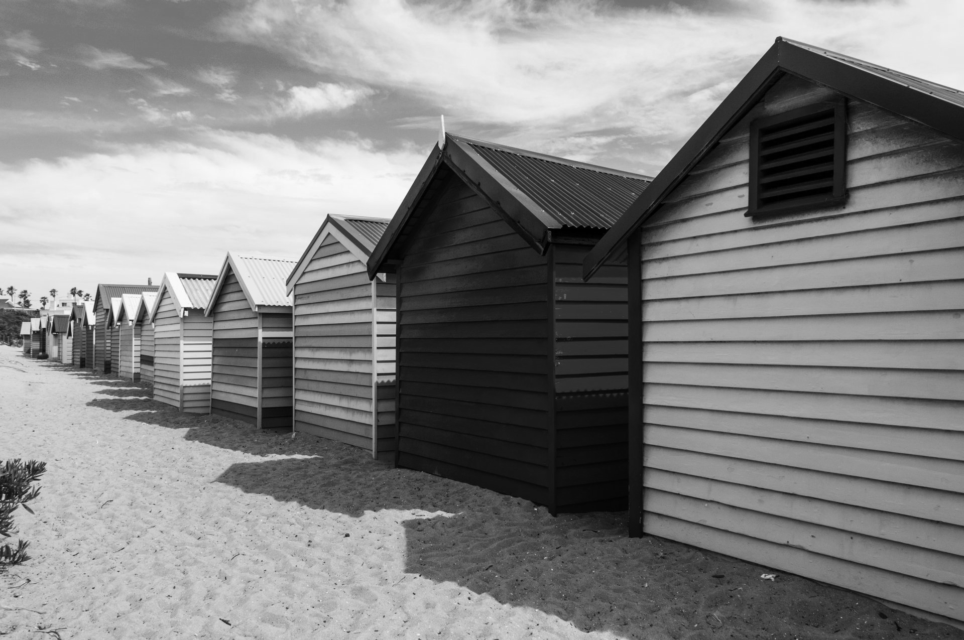 Fileira de cabanas de praia coloridas em uma praia de areia, com sombras projetadas na areia.