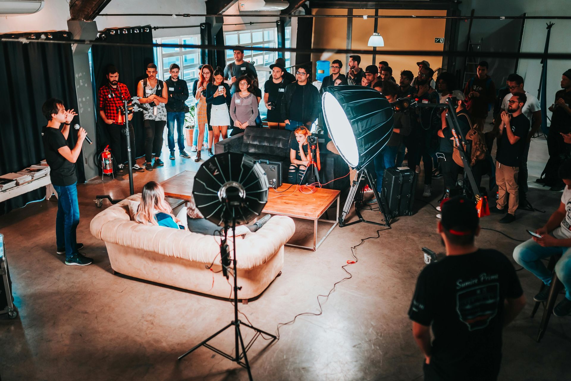 Indoor photoshoot with softbox lights, a model on a couch, and a crowd watching in a studio