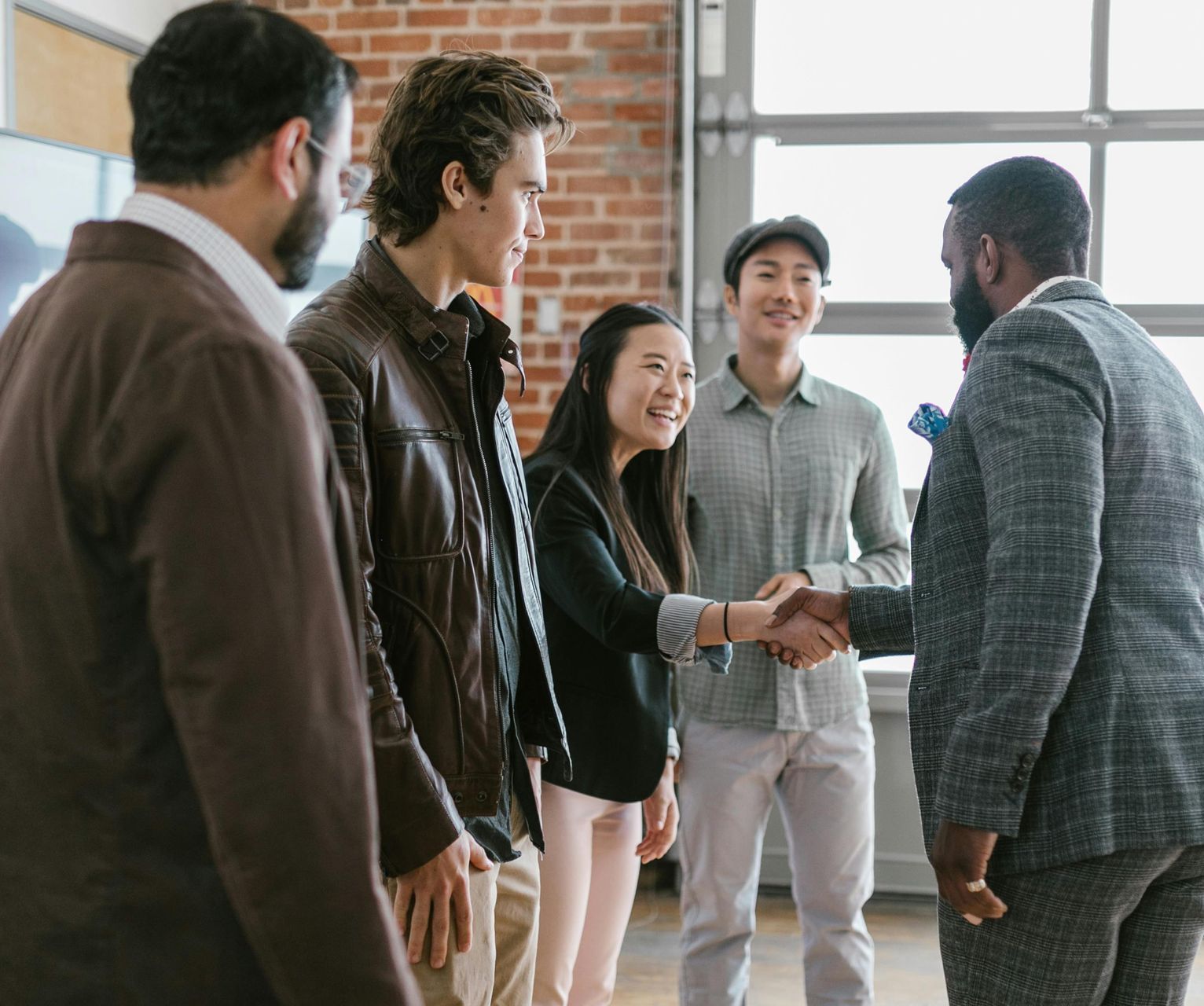 Five coworkers shaking hands and smiling in a bright office lounge