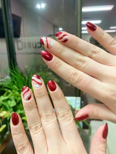 Hands with almond-shaped nails. Red polish on most, while some have red and white swirled designs.