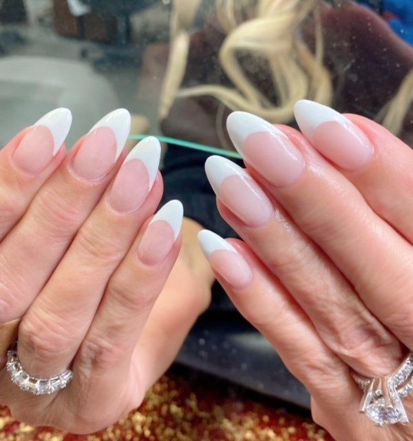 Hands with almond-shaped French tip nails, wearing diamond rings.