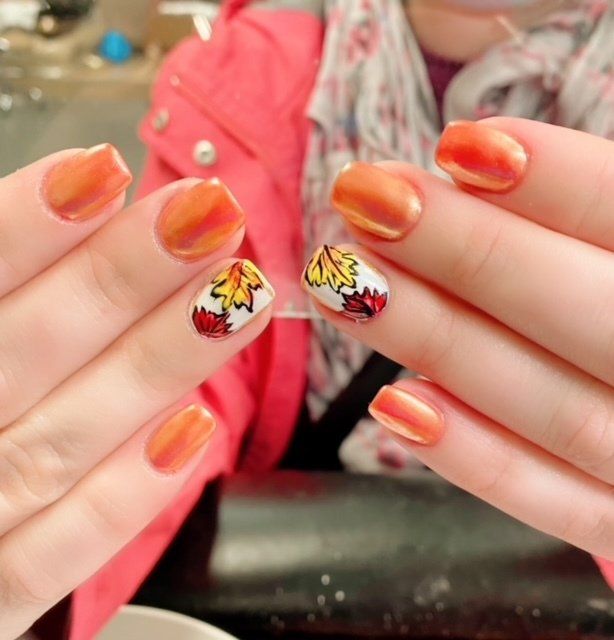 Orange nails with autumn leaf art.