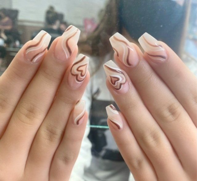 Hands with coffin-shaped nails. Light pink base with brown swirls and heart designs.