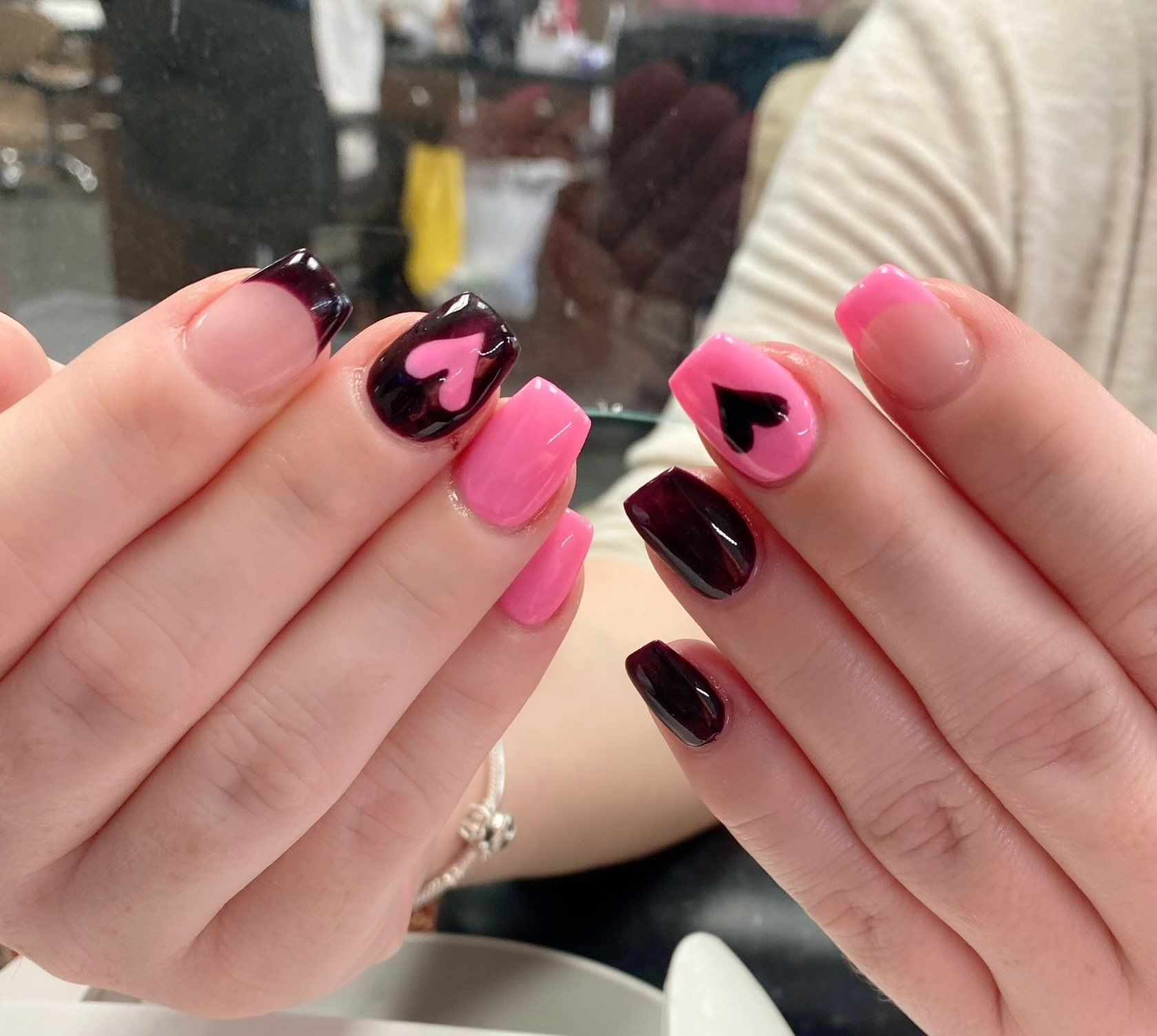 Hands displaying Valentine's Day-themed nails: pink, dark red, and heart accents.
