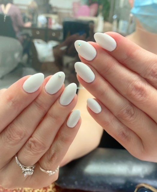 Hands with oval, matte white nails and sparkling rings.