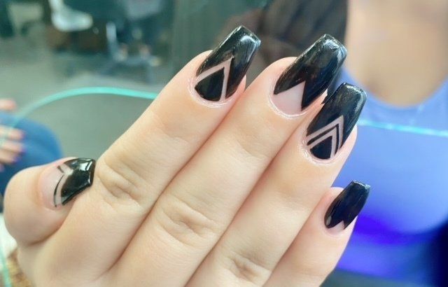 Hand with long, black, geometric nail art: black and clear triangles.