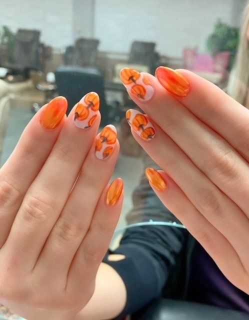 Hands with orange, pumpkin-themed nail art, including pumpkins on a white background.