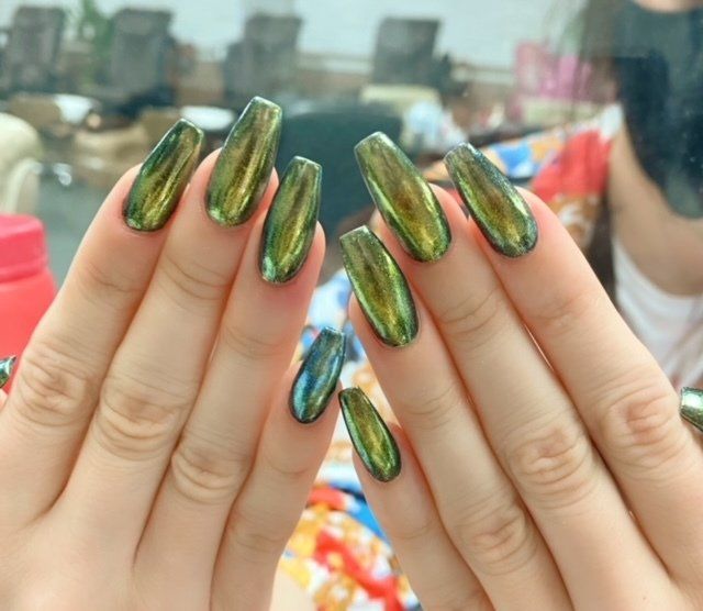 Hands with long, glossy green-gold metallic nails, reflecting light.