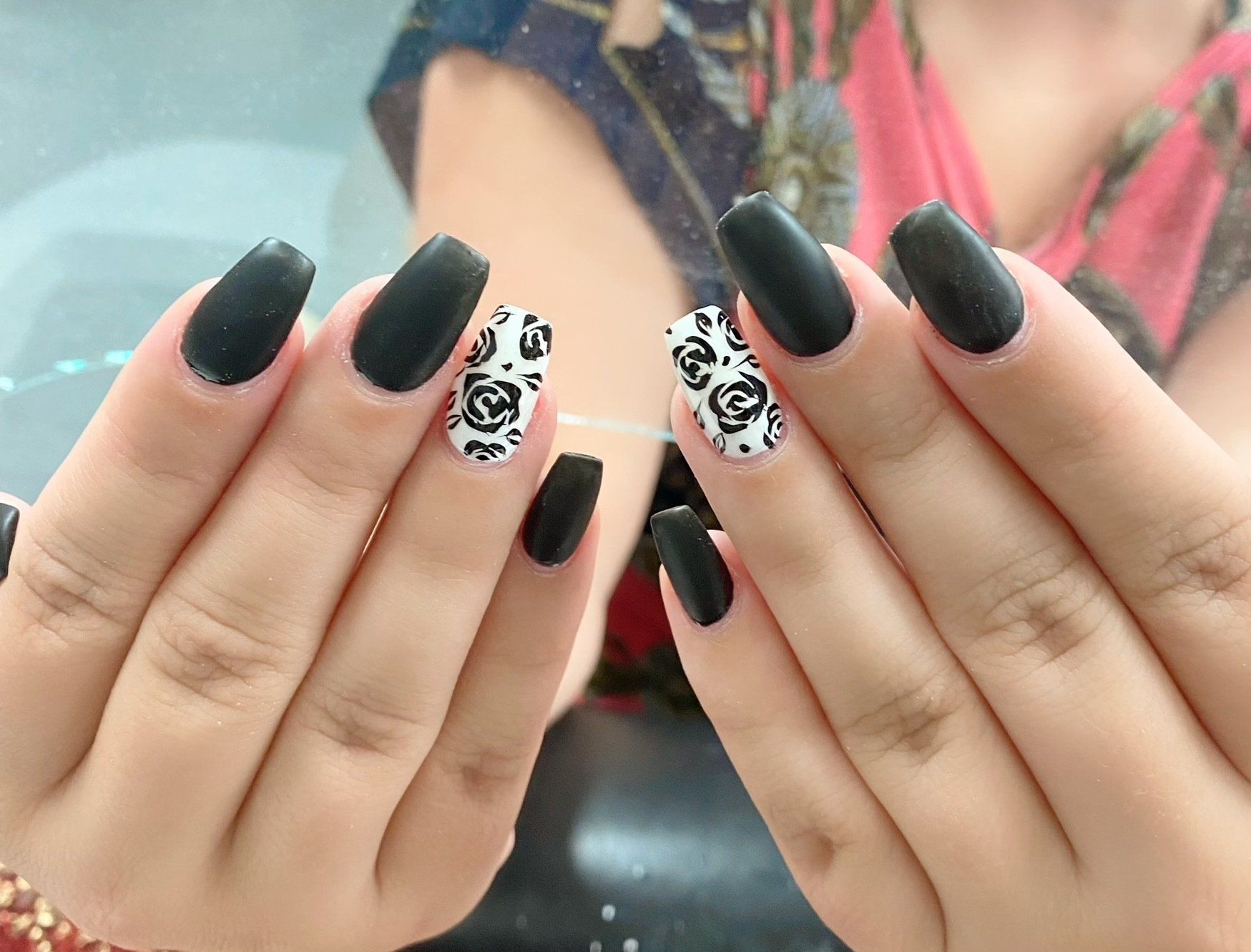 Hands with coffin-shaped black matte nails. Two nails have white rose pattern.