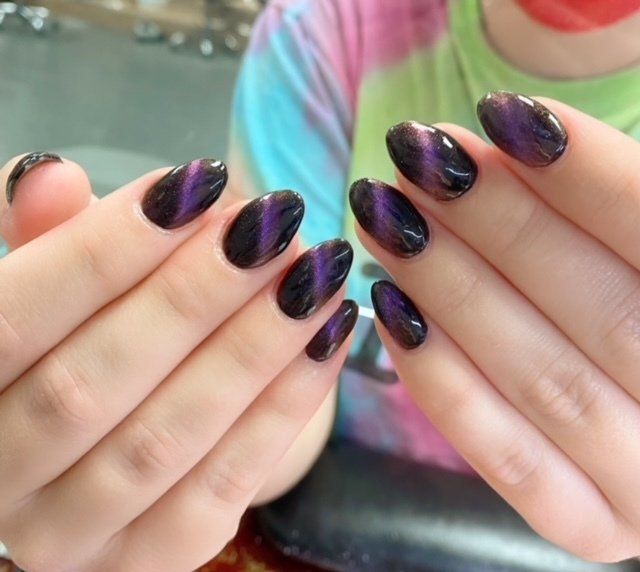 Hands displaying oval-shaped nails with a cat-eye effect, purple and black.