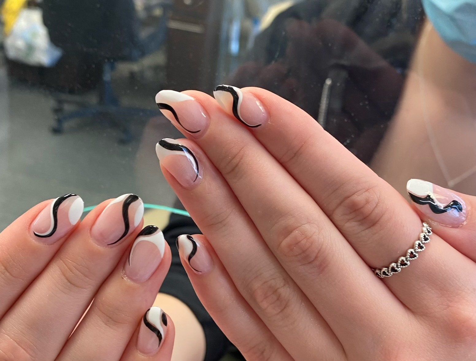 Woman's hands with oval-shaped nails painted with white, clear, and black wavy designs.