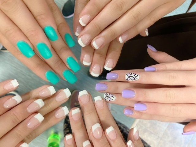 Hands with manicured nails in various colors: teal, white French tips, and lavender.
