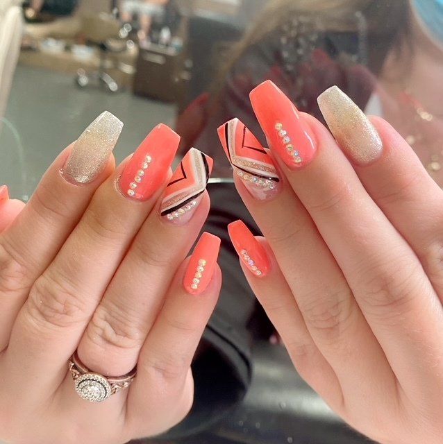Hands with coral-colored coffin nails. One hand has a ring. Some nails have glitter and lines.
