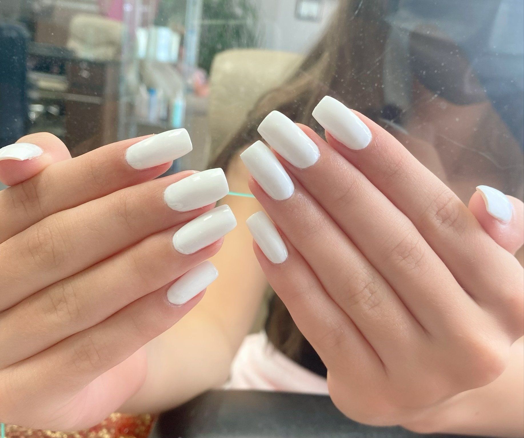 Hands with white square-shaped acrylic nails, posed in front of a mirror.