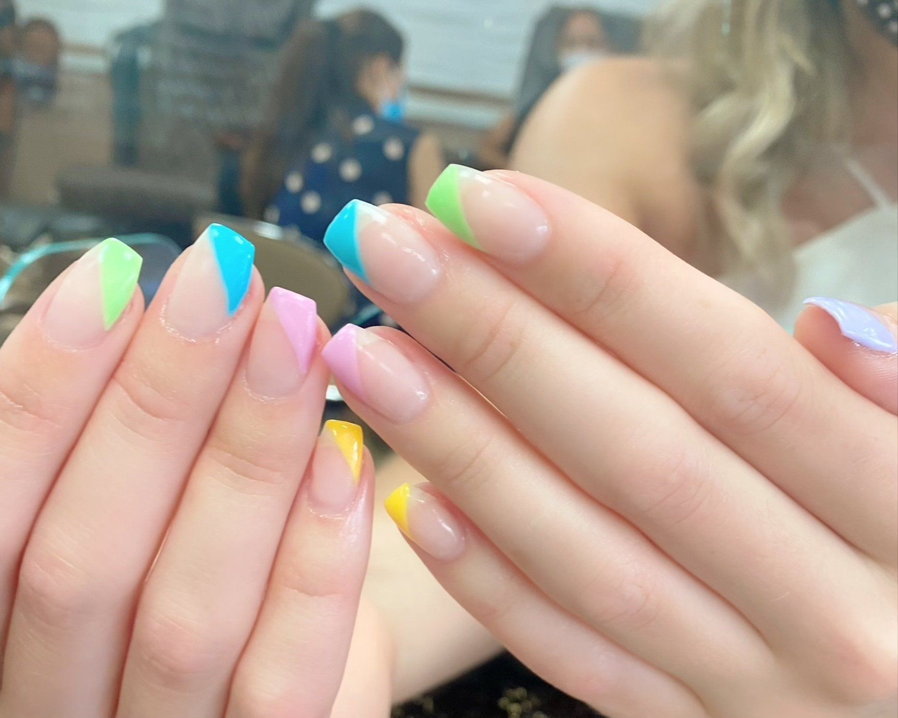 Hands with pastel-colored French tip nails in a salon setting.